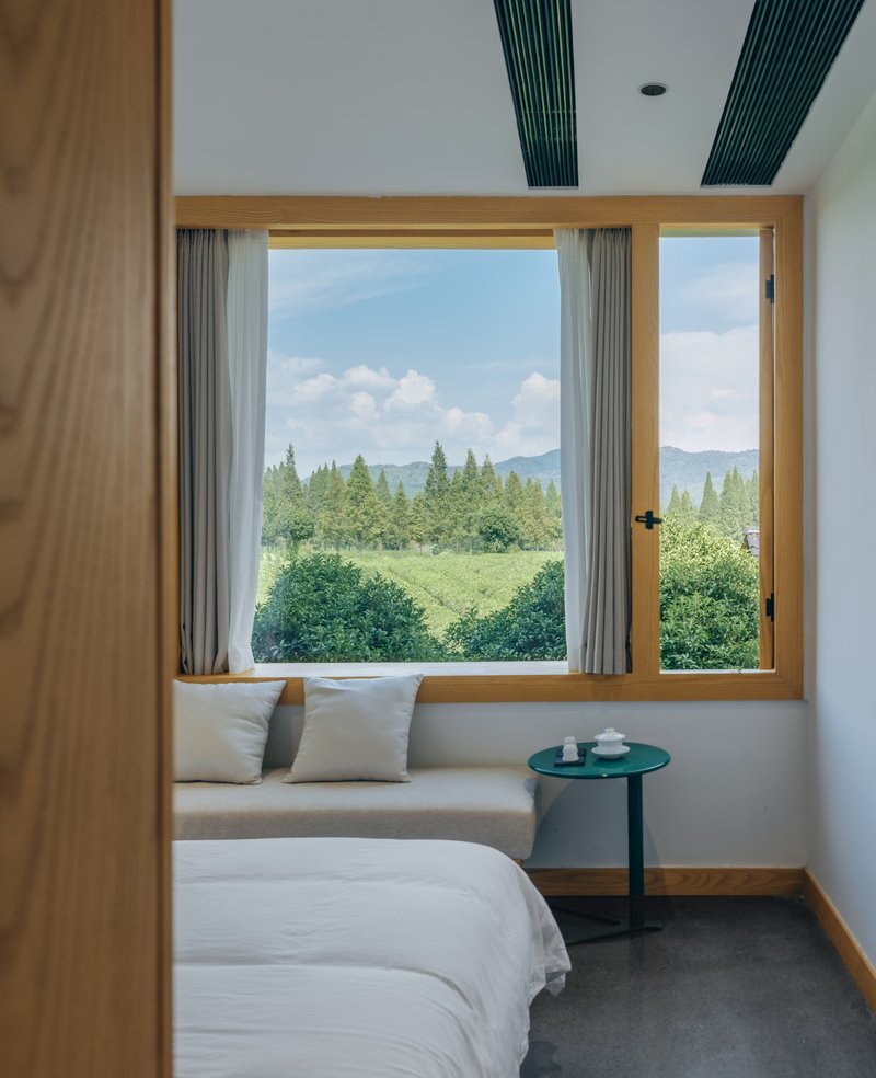 Bedroom with timber-framed window seat overlooking tea plantation and distant mountains on a partly cloudy day