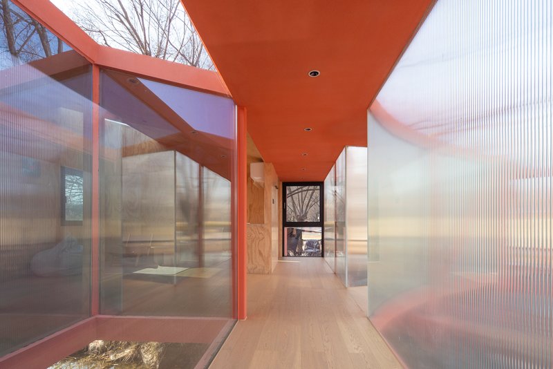 Corridor view with orange painted soffit and translucent corrugated walls flanking a planted courtyard