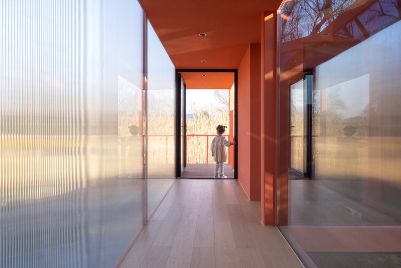 Interior corridor with fluted glass walls and a figure silhouetted in the doorway to the landscape