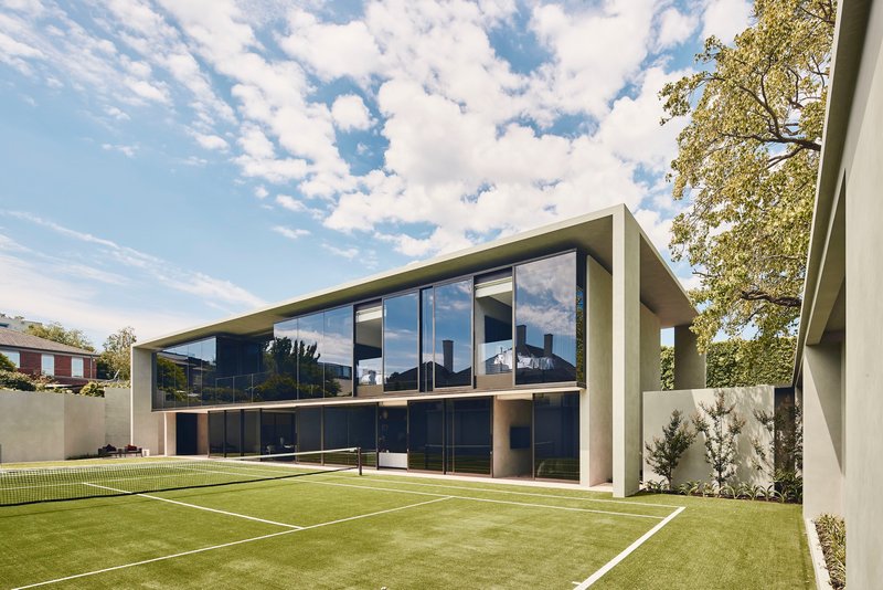 Rear elevation with floor-to-ceiling glazing overlooking a tennis court with synthetic grass surface