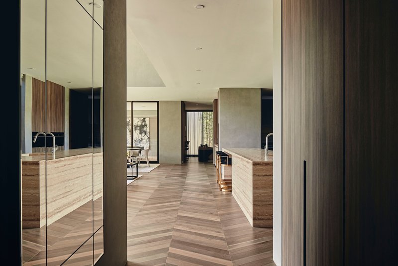 View through doorway into kitchen with chevron timber flooring and concrete wall panels