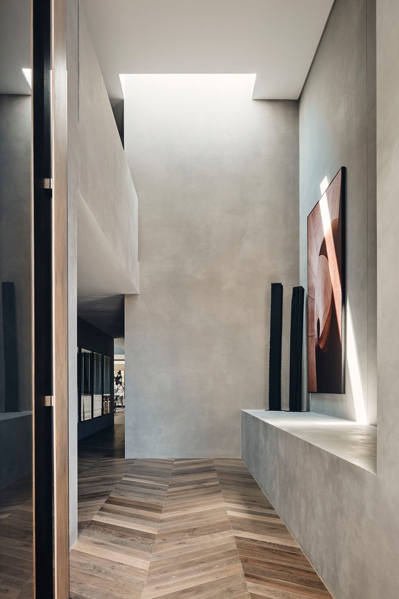 Corridor with herringbone timber floor, skylight above, and concrete bench displaying sculptures