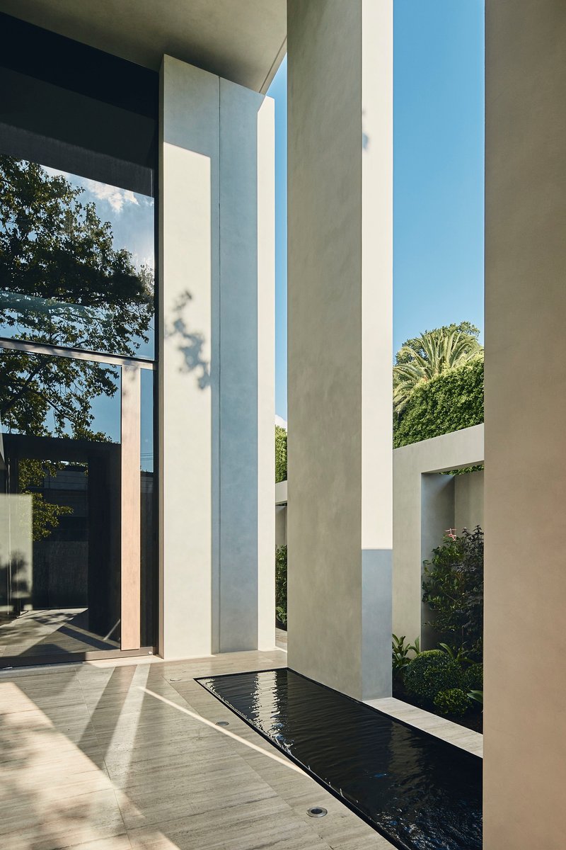 Concrete entry courtyard with tall vertical columns flanking a reflecting pool and planted beds