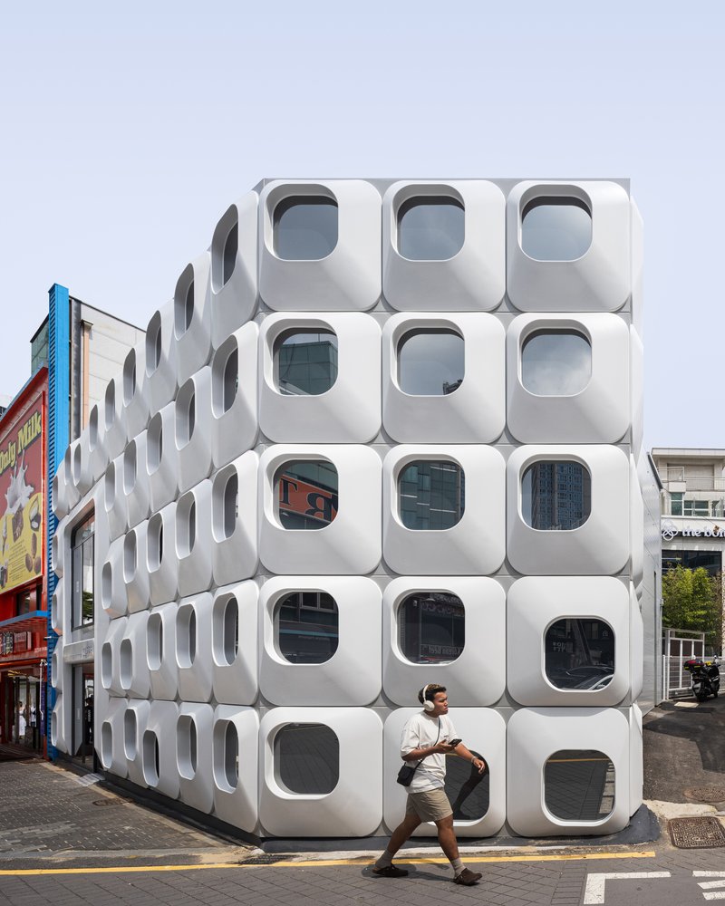 Corner facade showing stacked white modules with porthole windows as a person passes in front