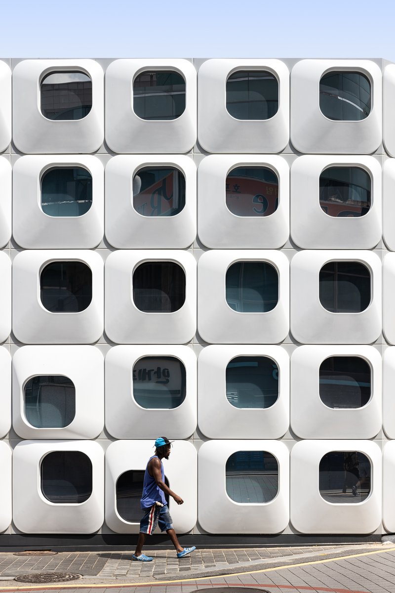 Grid of rounded square window modules with a person walking past on the pavement below
