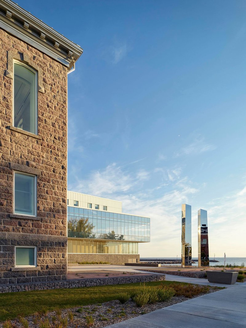 Historic masonry tower beside the glass addition with carved totem poles in the lawn