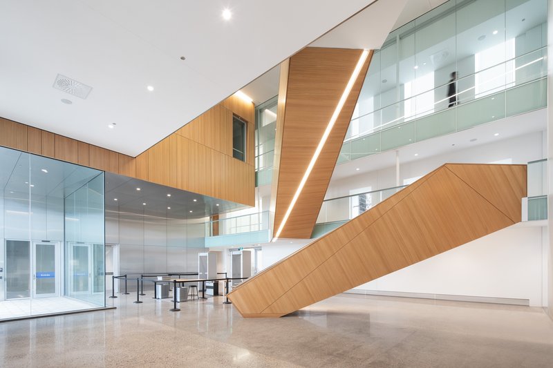 Multi-level lobby with diagonal timber staircase featuring integrated lighting and glass balustrades on upper level