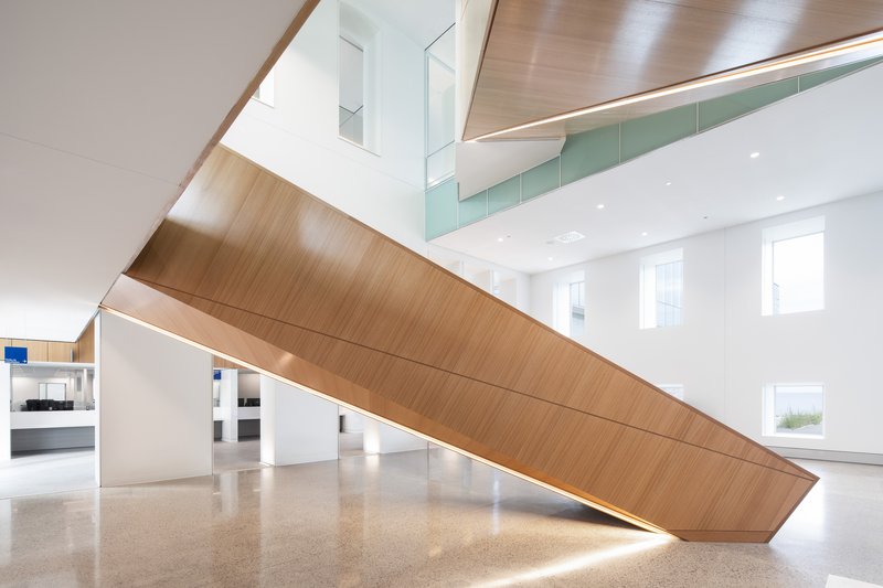Tilted timber-clad staircase with integrated lighting rising through a double-height lobby with terrazzo flooring