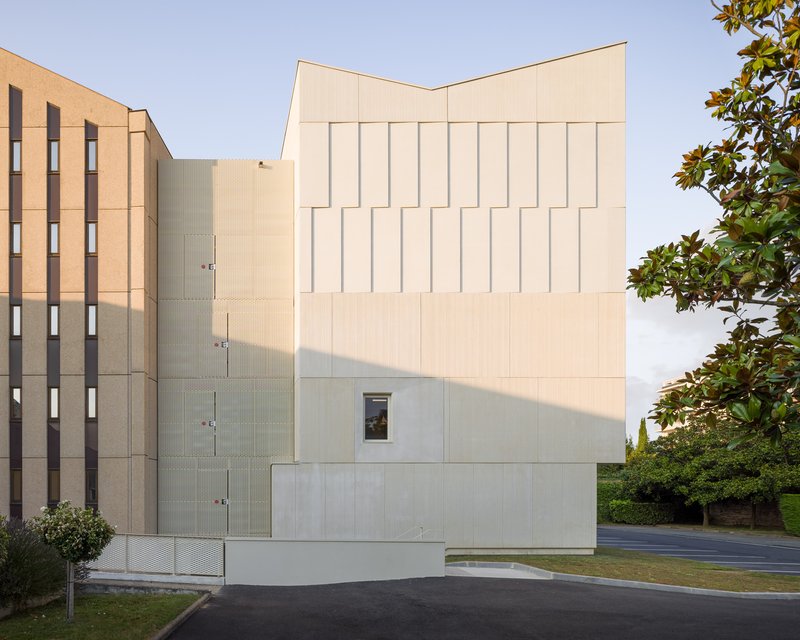 Rear elevation showing the faceted white facade in warm afternoon light with adjacent residential tower