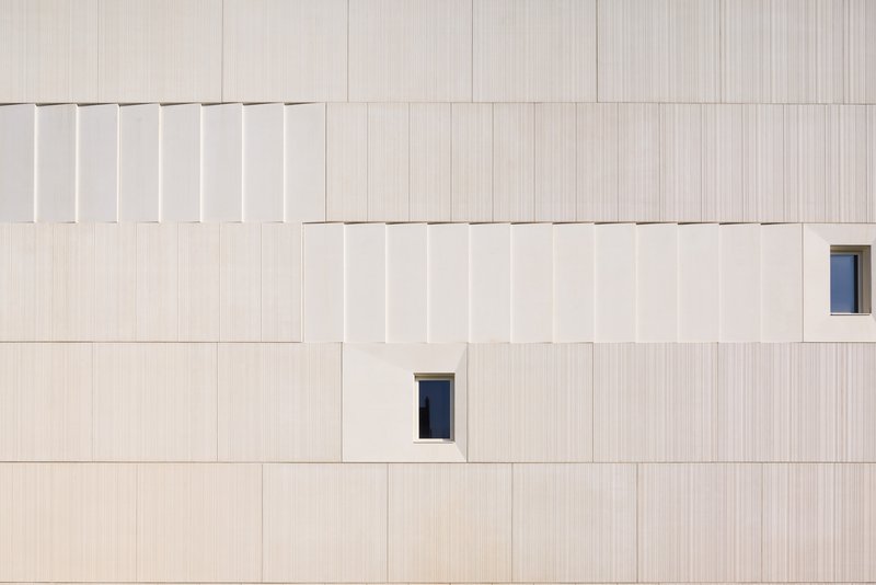 Facade detail showing vertically striated panels with offset joints and two small rectangular window openings