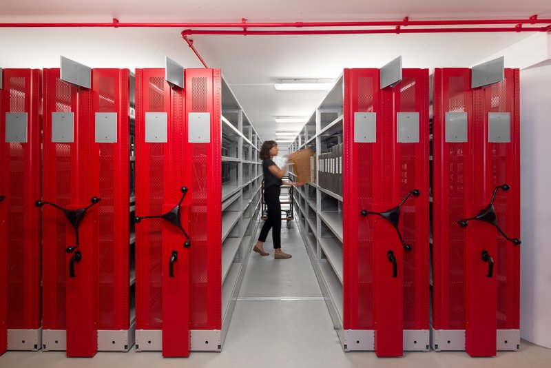 Aisle view of red mobile shelving units with perforated panels as a person walks through