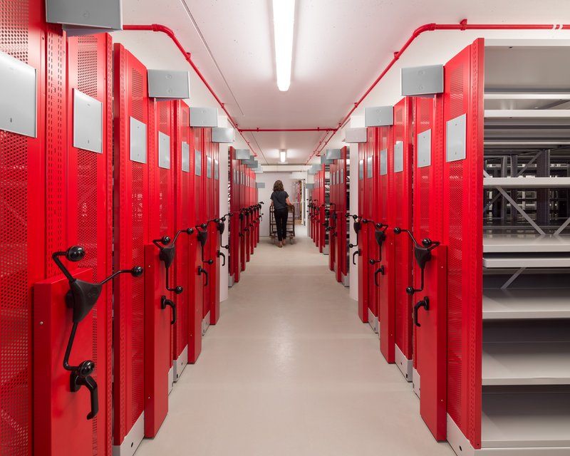 Red mobile shelving corridor with exposed conduit on ceiling and person in distance