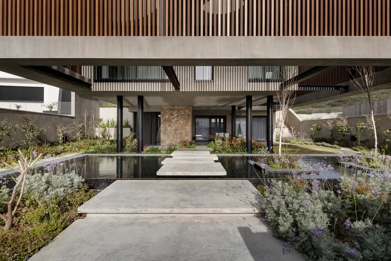 Entry pathway bridging reflecting pools beneath slatted timber soffit and black steel columns