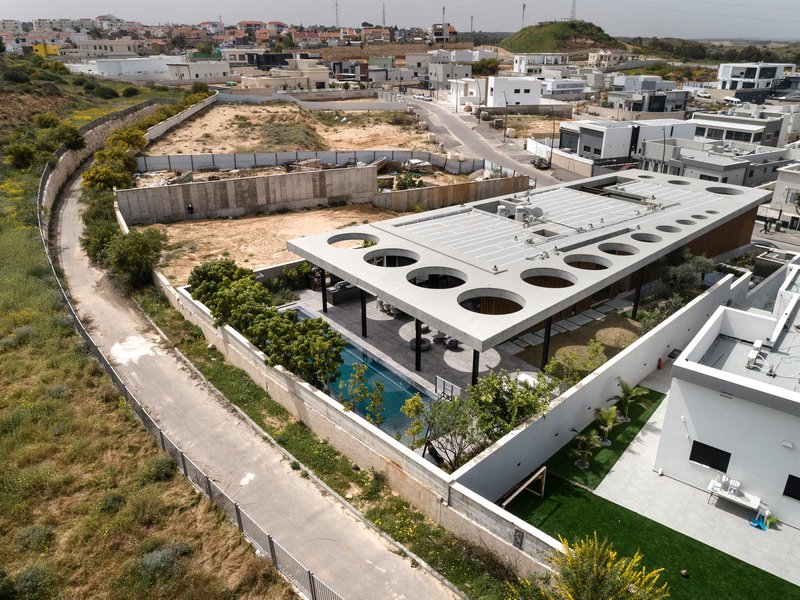 Aerial view of white concrete roof with circular voids over terraced gardens in hillside neighborhood