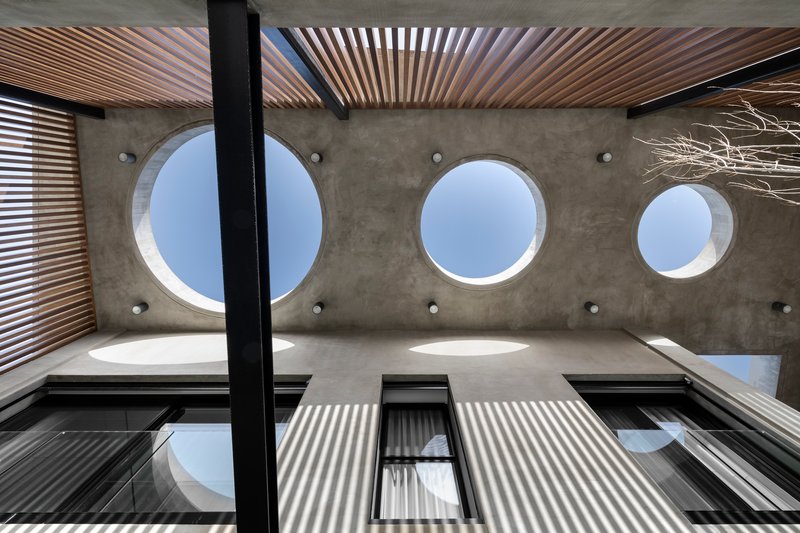 Upward view of concrete ceiling with circular skylights and timber louvered screens casting shadow patterns