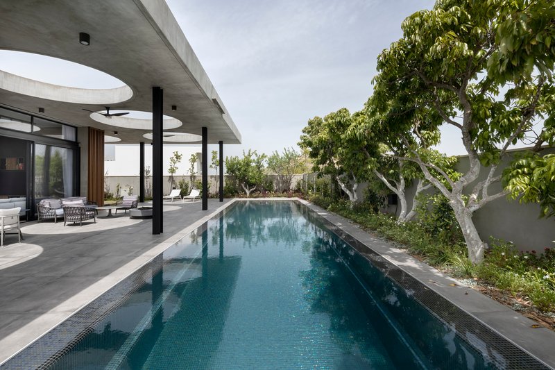 Long lap pool bordered by paving and mature trees under a concrete canopy with circular skylights