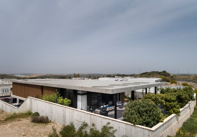 Corner view showing the timber-clad facade behind the concrete base wall with scattered vegetation