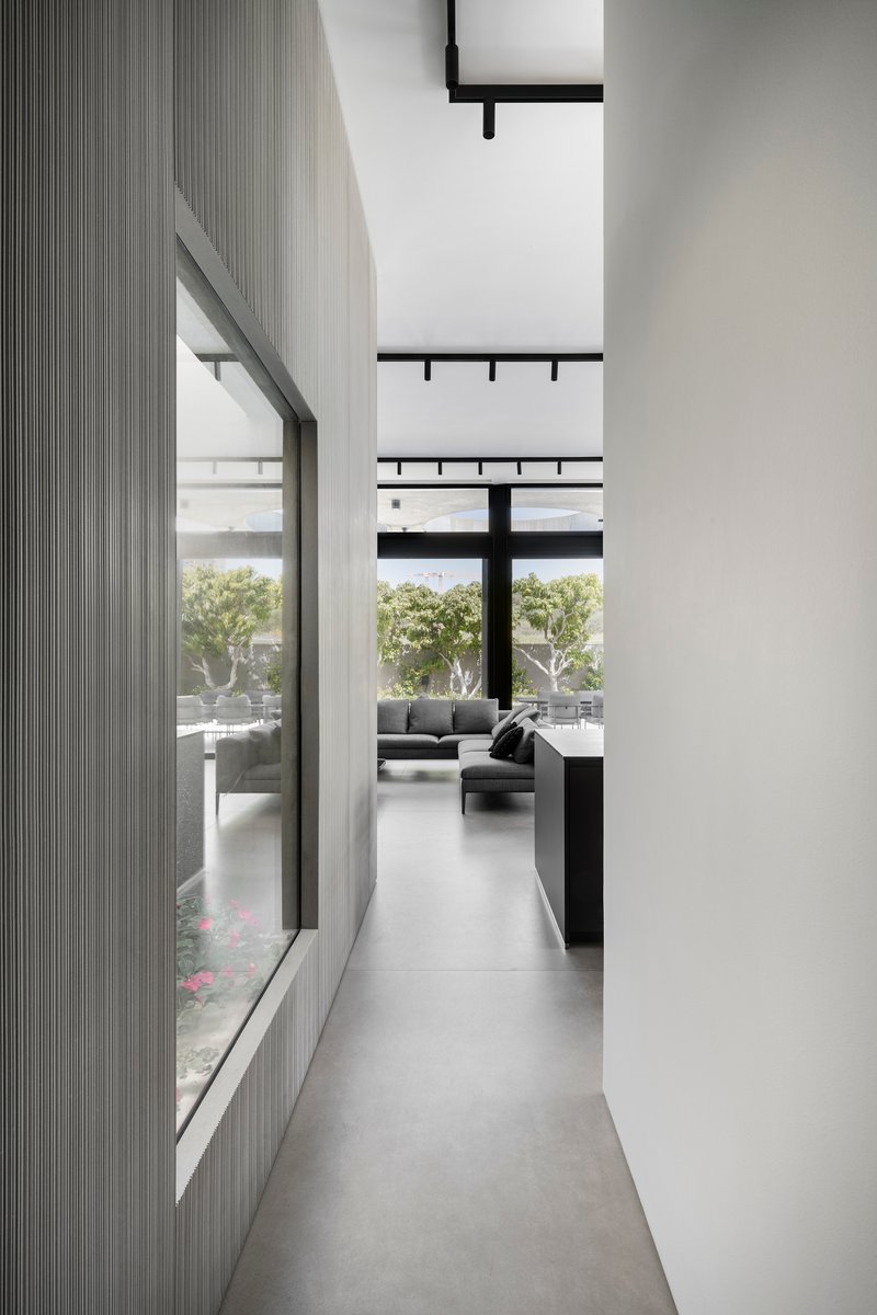Narrow corridor with fluted grey wall panels and high clerestory windows overlooking a planted courtyard