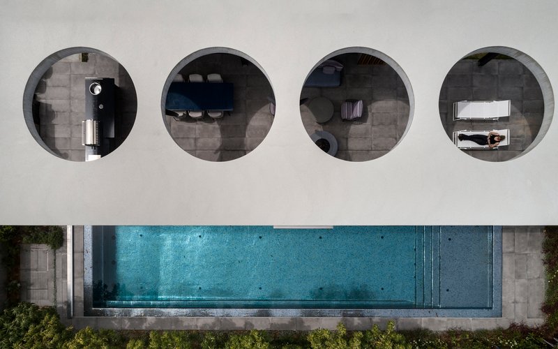 Overhead view of four circular openings in a white roof revealing interior spaces and a lap pool below