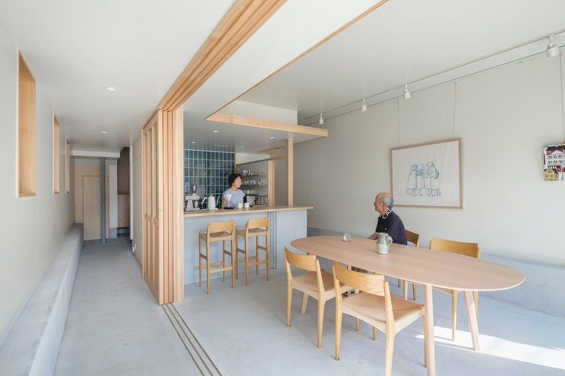Open kitchen with timber slat partition and dining table where two residents sit and stand