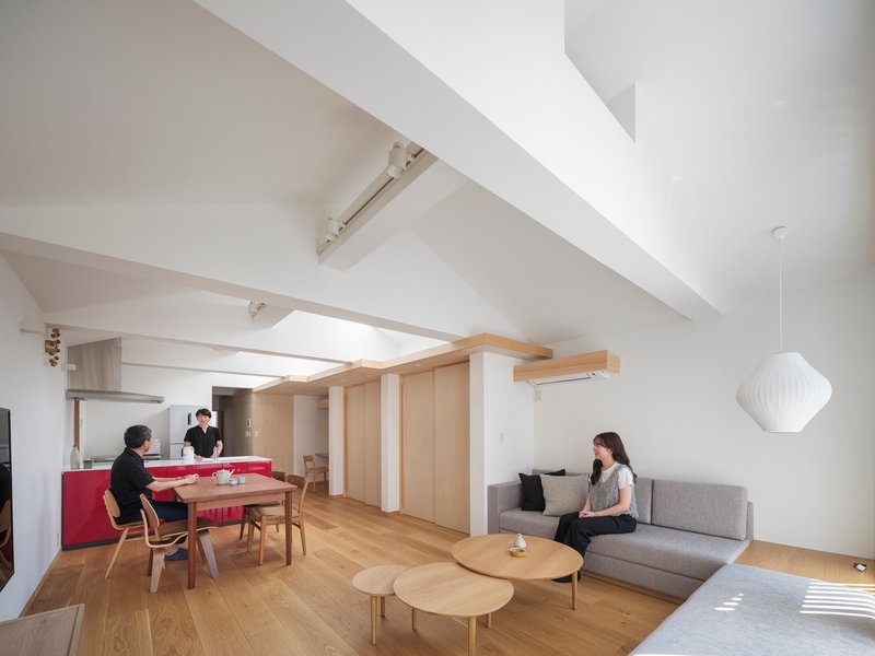 Open-plan living space with residents at dining table and kitchen under angled skylight