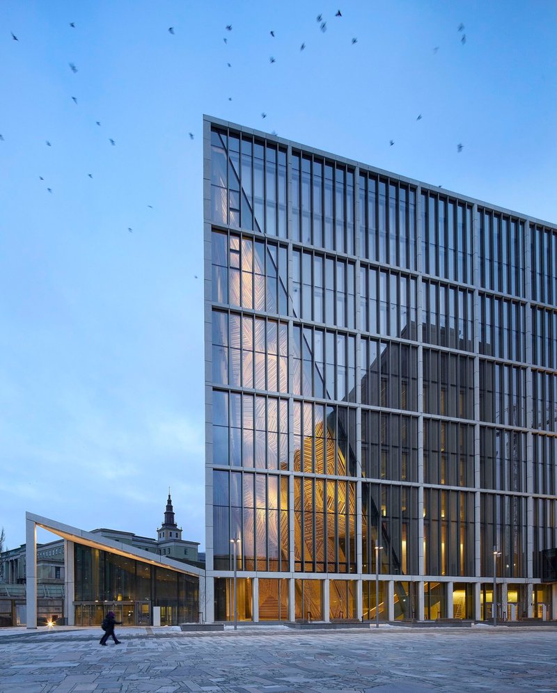 Glass facade reflecting the timber-clad atrium and surrounding buildings at dusk with birds overhead