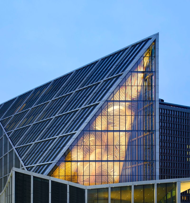 Triangular glass gable revealing illuminated timber-lined interior at twilight