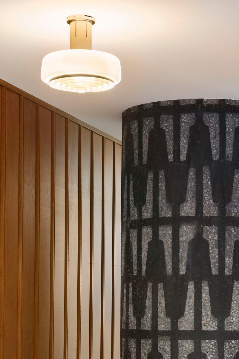 Flush-mounted white glass pendant light with brass fitting above vertical wood paneling and patterned dark wallcovering