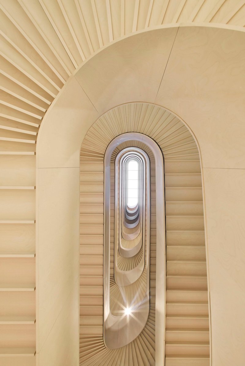 Upward view through oval stairwell with radiating handrails and skylight at summit creating bright central glow