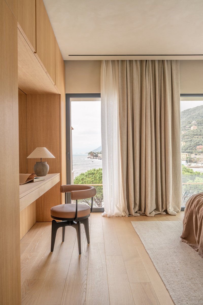 Built-in oak desk and chair beside a window overlooking coastal hills in afternoon light