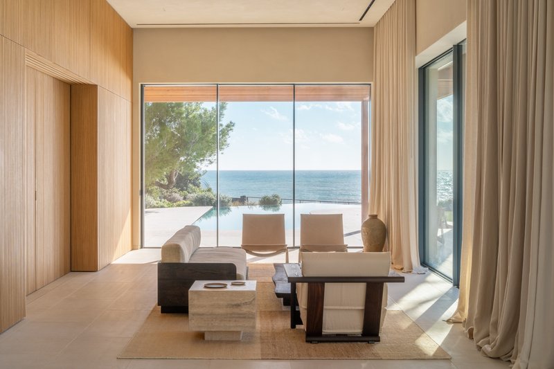Living room framed by wood paneling with full-height glazing opening to a terrace and ocean view