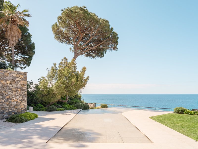 Stone wall and paved terrace extending toward the pool and coastline under a clear sky