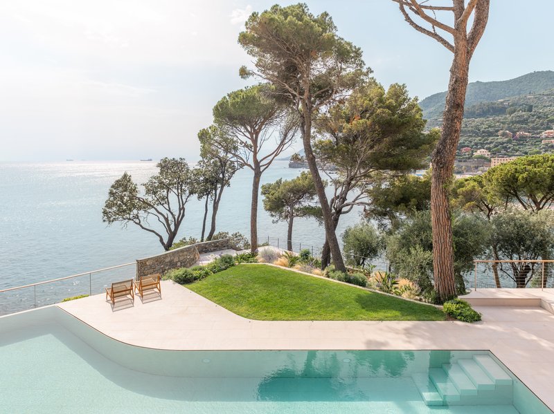 Curved infinity pool edge with lawn and mature pine trees overlooking the sea