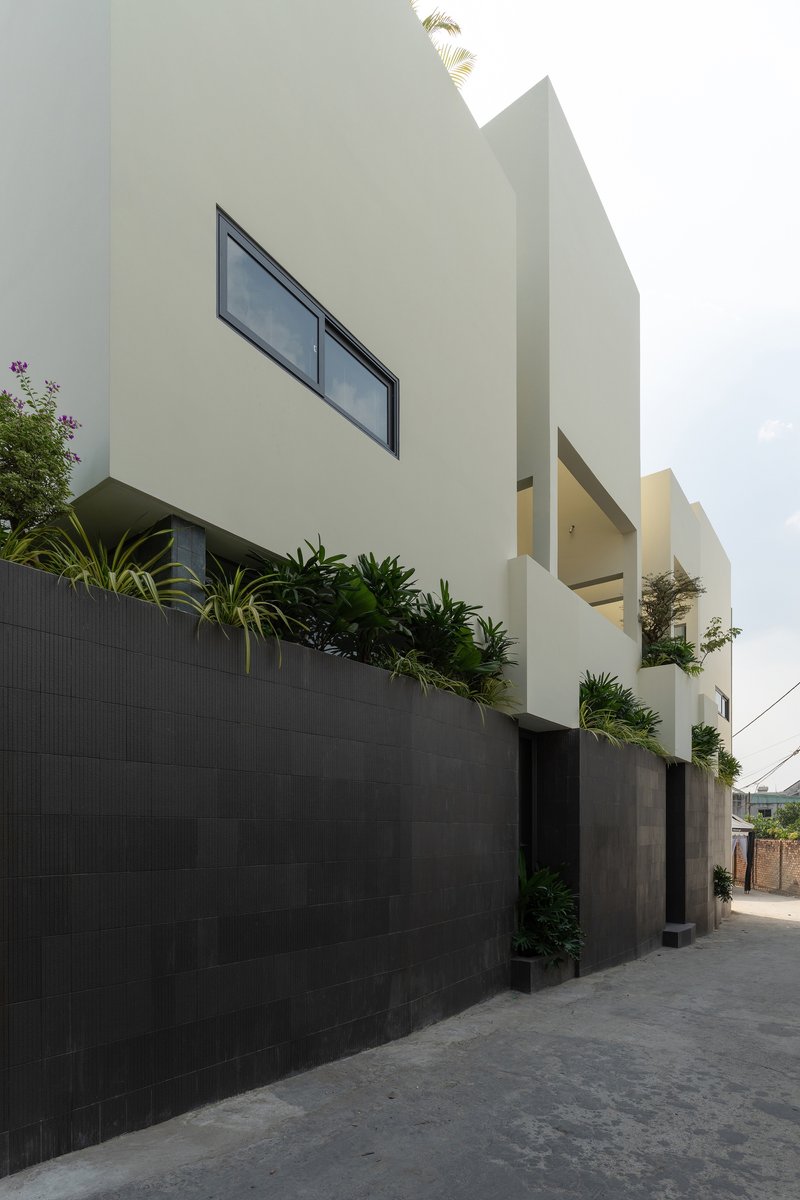Street facade showing white geometric volumes rising above a dark tiled boundary wall with planted beds