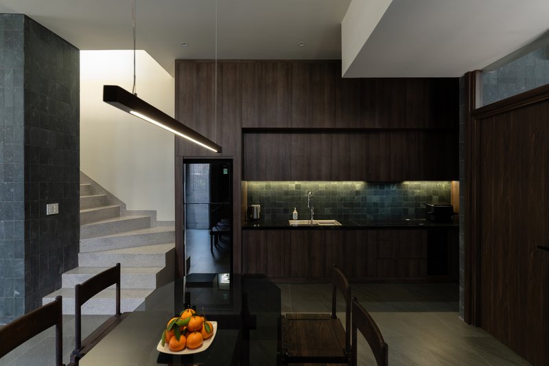 Open kitchen with dark wood cabinetry and under-cabinet lighting beside a concrete staircase with a fruit bowl