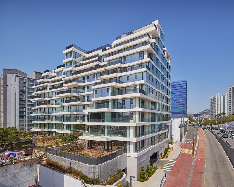 Street corner view showing the offset white balconies and glazed facade beside a roadway with traffic