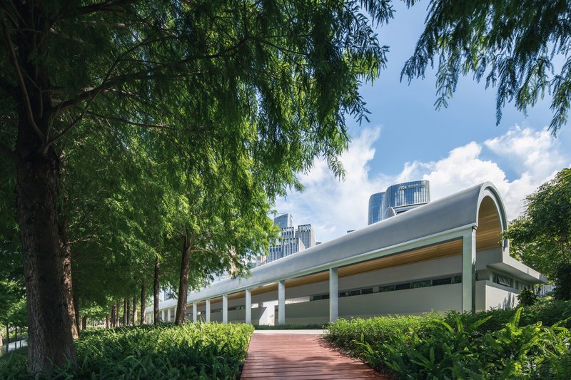 Barrel-vaulted roof above a colonnade entry plaza framed by willow trees and trimmed hedges