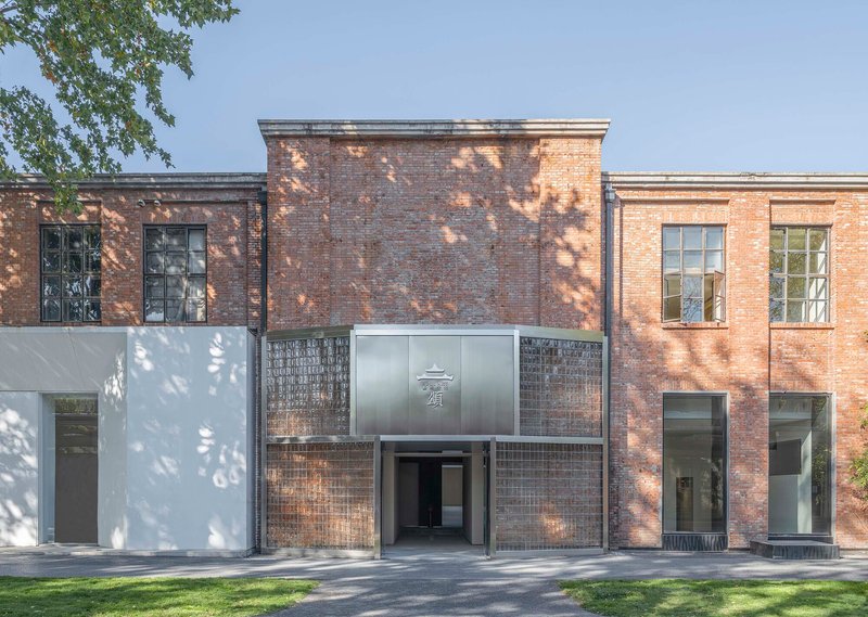 Front facade combining dark brick volumes with white stucco and glass brick under dappled tree shadow