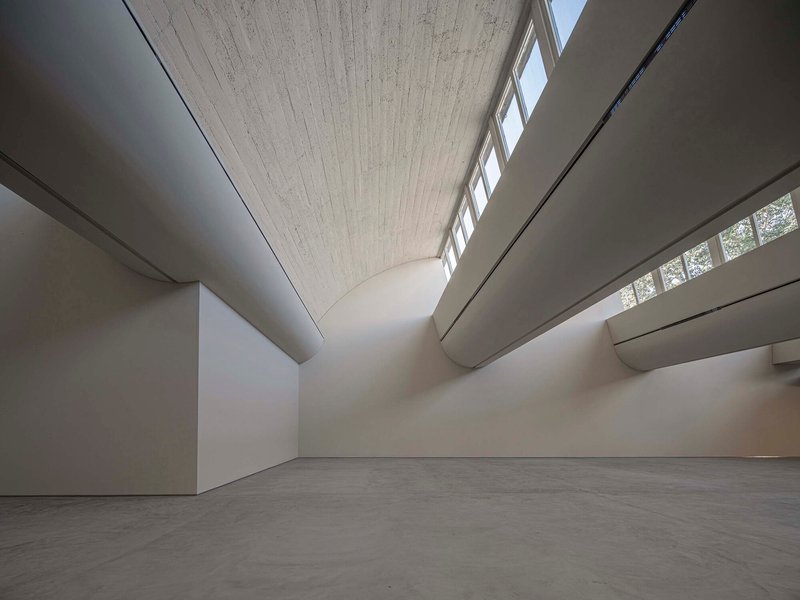 Gallery space showing vaulted wood ceiling with clerestory bands and curved white walls meeting concrete floor