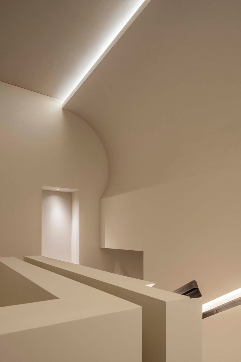 Stairwell with vaulted ceiling, recessed linear lighting and geometric white plaster volumes