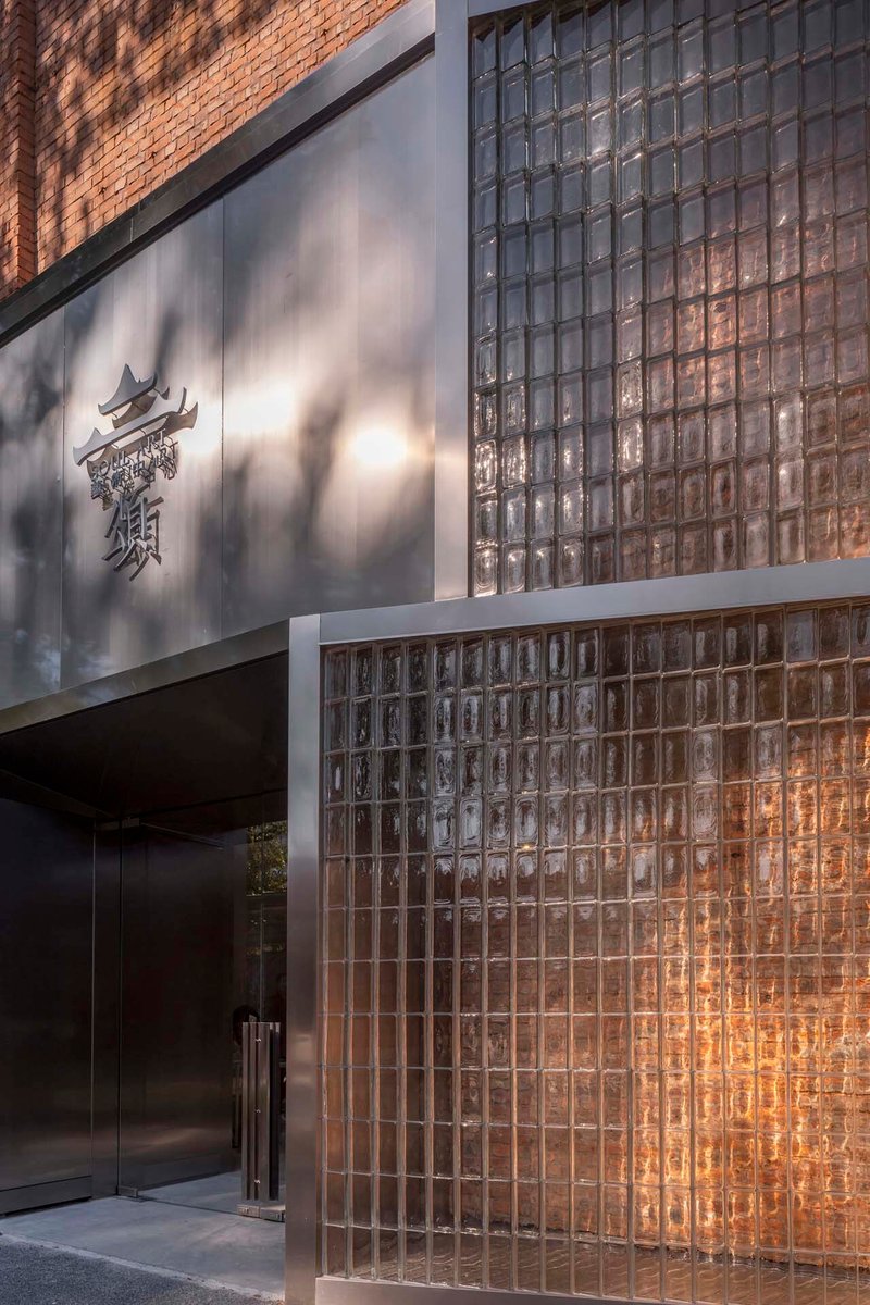 Street-level entrance with glass block facade and grey metal panel above bearing a sculpted logo