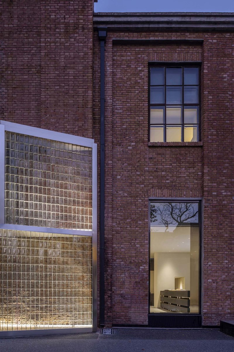 Glass block facade framed in metal against brown brick walls with tall windows at dusk
