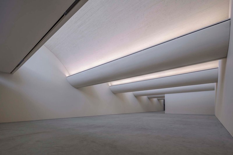 Interior gallery space with stepped ceiling planes creating receding layers of indirect light above polished floor