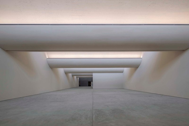 Gallery corridor with telescoping ceiling recesses and concealed lighting drawing the eye toward a distant opening