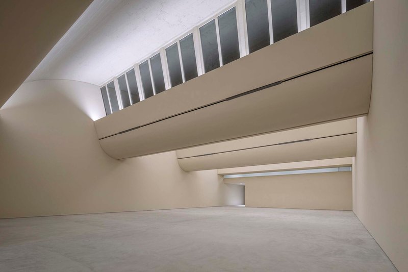 Gallery space with curved ceiling and horizontal clerestory admitting daylight above layered wall planes