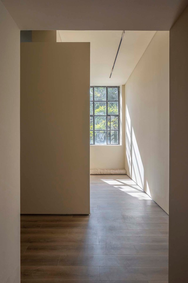 View through doorway toward steel-framed window with dappled sunlight on wood floor