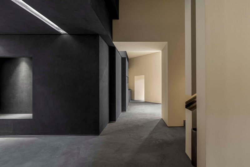 Circulation corridor between black metallic walls and cream partitions with polished concrete floor