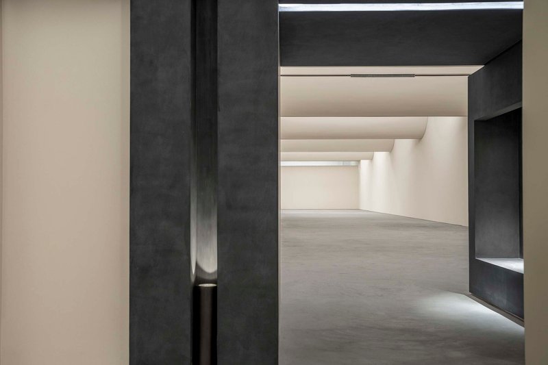 Doorway framed by dark concrete portal opening into a gallery space with recessed ceiling coves