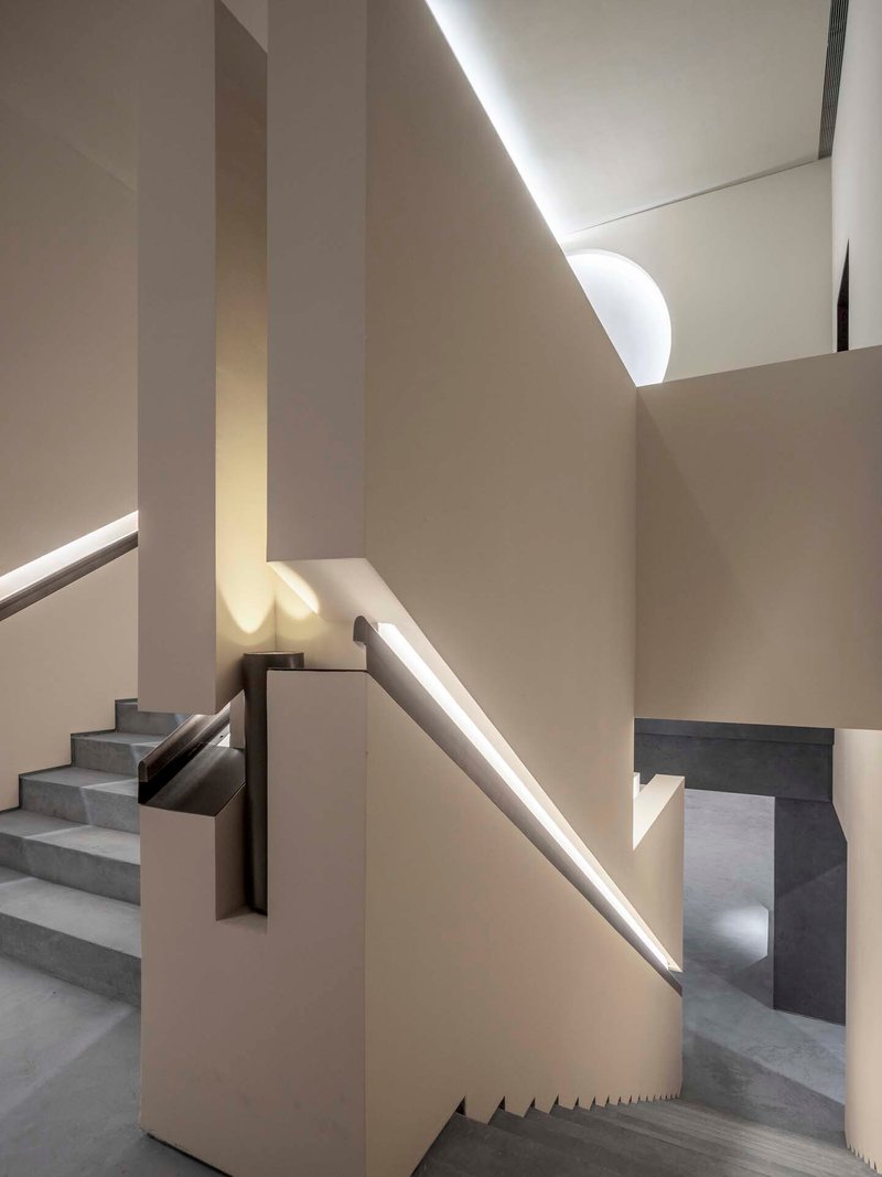 Concrete staircase with integrated LED handrail lighting ascending between cream plaster walls and skylights