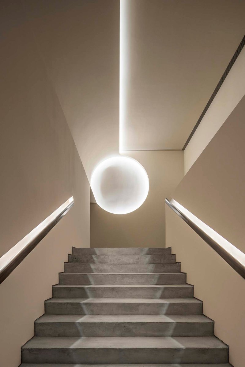 Upward view of concrete stair with spherical pendant light and illuminated ceiling slot above